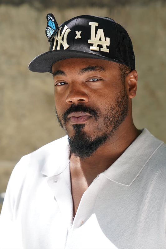 Man wearing a black cap with a NY X LA logo and butterfly, looking to the side.